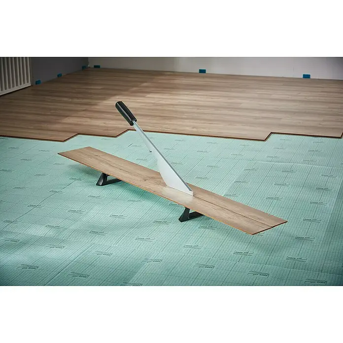 Wolfcraft Cortaláminas de parquet LC 600 - Ancho de corte: 465 mm, Aluminio - Una herramienta para cortar suelos laminados está sobre una base verde, con suelos laminados al fondo.