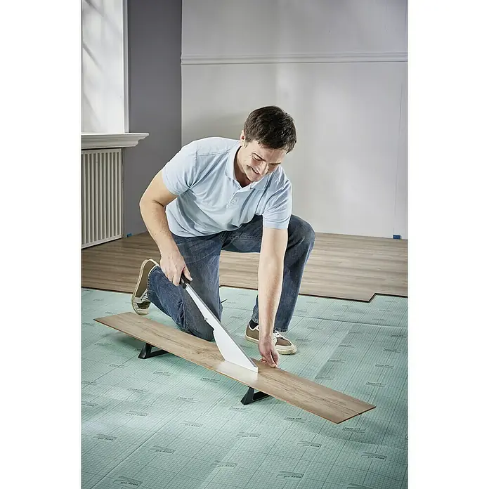 Wolfcraft Laminatschneider LC 600 - Geeignet für: Laminat, Schnittbreite: 465 mm, Material: Aluminium - Ein Mann kniet und schneidet Laminat mit einer Laminatschneidemaschine auf einer grünen Unterlage.