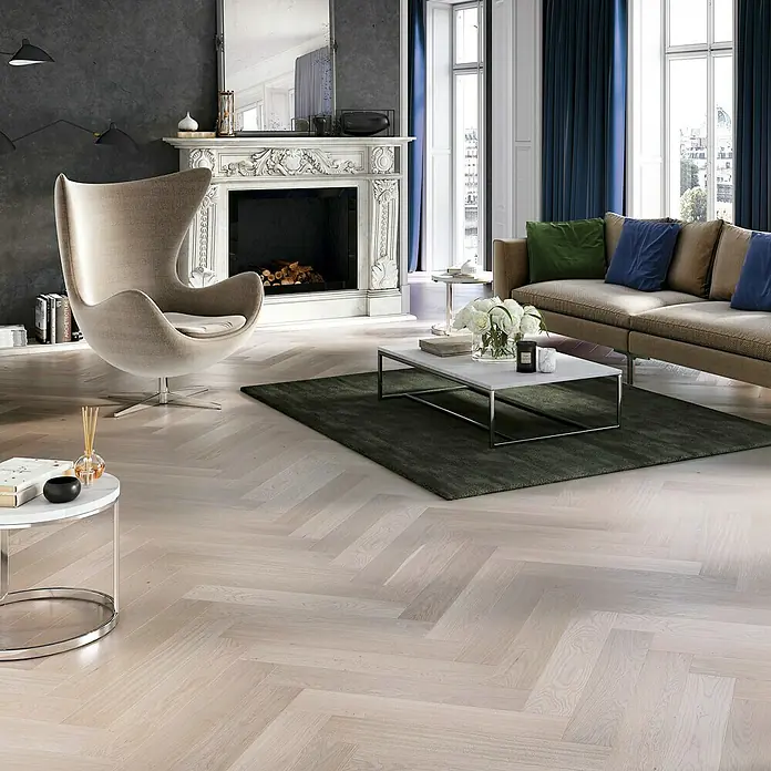 Barlinek Parkett Classico Line - Eiche Marzipan, Fischgrät, 725 x 130 x 14 mm - Elegantes Wohnzimmer mit hellem Fischgrätparkettboden, Sessel und Kamin. Die Diele verleiht dem Raum eine moderne und stilvolle Atmosphäre.
