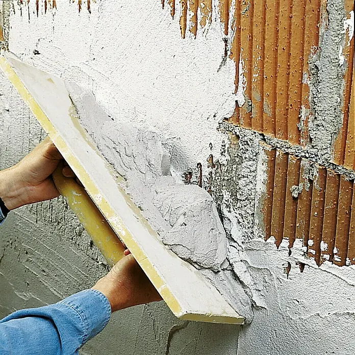 Knauf Rotband Haftputzgips - 30 kg - Auftragen von Putz auf eine Ziegelwand mit einer Kelle. Die Kelle ist mit frischem Putz bedeckt, der auf die Wand aufgetragen wird.