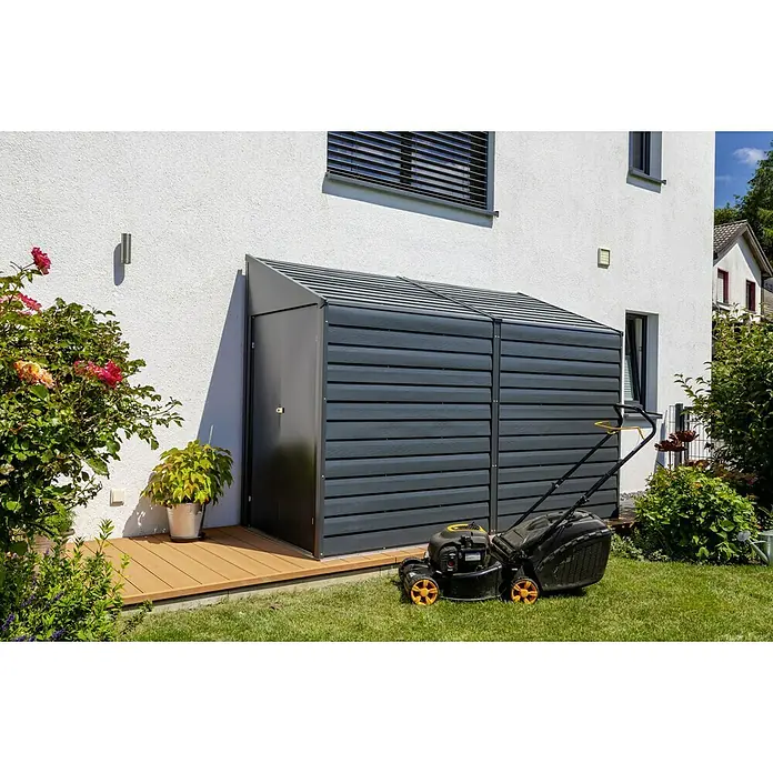Spacemaker Gerätehaus 4x10 - Außenmaß inkl. Dachüberstand (B x T): 124,5 x 294,6 cm, Stahl, Grau - Graue Gartenbox aus Holz neben einem Rasenmäher vor einem Haus. Ideale Aufbewahrungslösung für Gartengeräte und Zubehör.