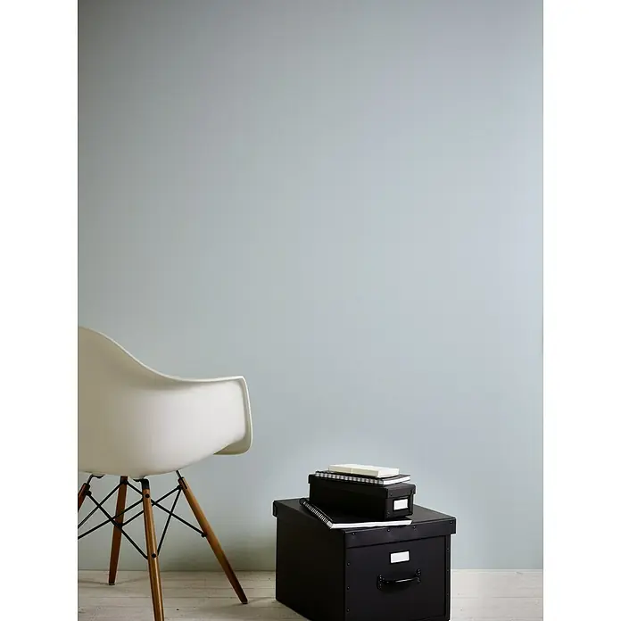 A.S. Création Flavour Vliestapete II - Hellblau, Uni, 10,05 x 0,53 m - Ein stilvolles Interieur mit einem modernen weißen Stuhl und schwarzen Aufbewahrungsboxen, ideal für Büro oder Zuhause. Die graue Wandfarbe sorgt für eine ruhige Atmosphäre.
