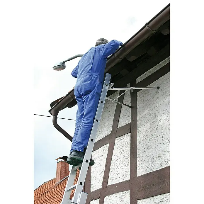 Krause Combi AbstandhalterGeeignet für: Holmquerschnitt 64 x 25 mm bis 97 x 25 mm, Aluminium - Mann auf einer Leiter, der die Dachrinne eines Hauses inspiziert. Die Leiter ist aus Aluminium und steht sicher am Haus.