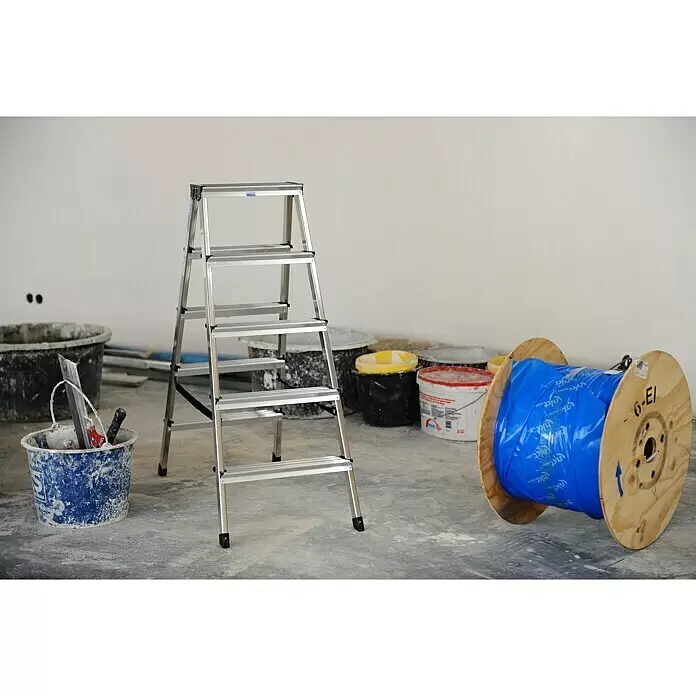 Krause Monto Escalera de tijera de doble acceso - Altura de trabajo: 2,65 m, Número de peldaños: 10 ud., Carga soportada: 150 kg, Aluminio - Escalera de mano plegable de aluminio plateado en una obra, rodeada de cubos y un carrete de cable.