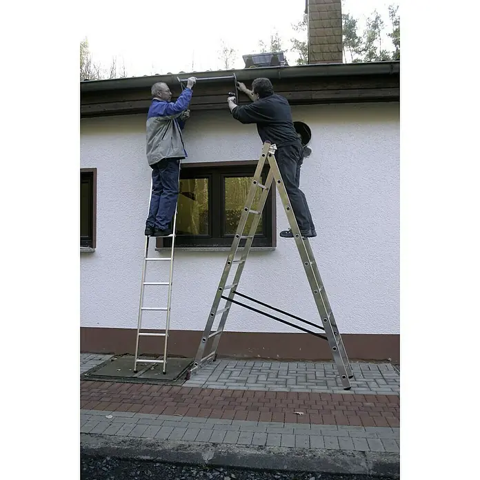 Krause Corda Escalera multiusos - Altura de trabajo: 6,2 m, Número de peldaños: 27 ud., Carga soportada: 150 kg, Aluminio - Dos hombres trabajan en escaleras en el lateral de una casa. Una escalera es plegable y la otra es una escalera normal.