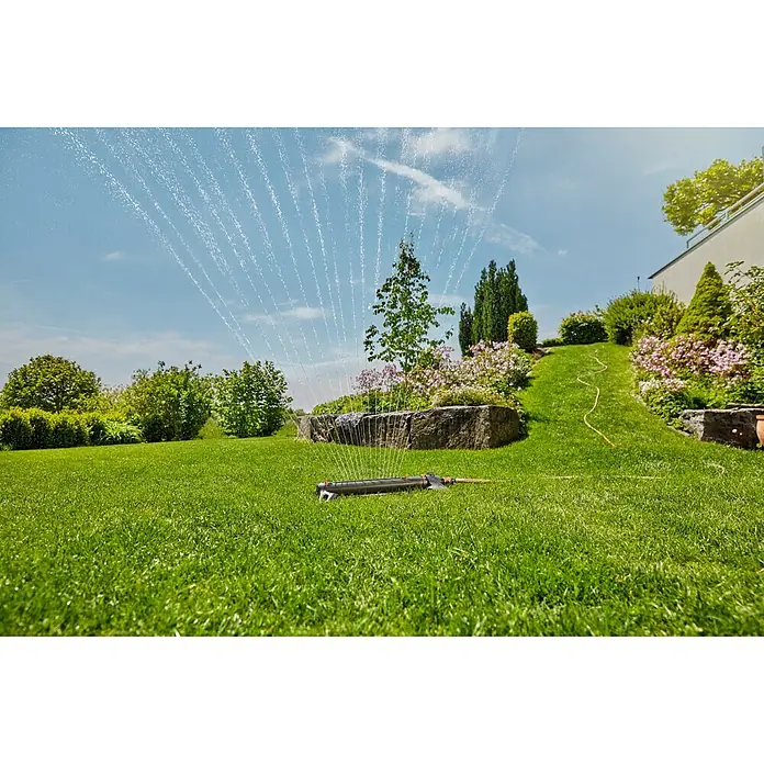 Gardena Viereckregner Aquazoom L - Max. Regnerfläche: 28 m² - 350 m² - Bild einer Vielflächenregner im Betrieb. Das Gerät bewässert einen Rasen mit vielen Wasserstrahlen, im Hintergrund ist ein Garten zu sehen.