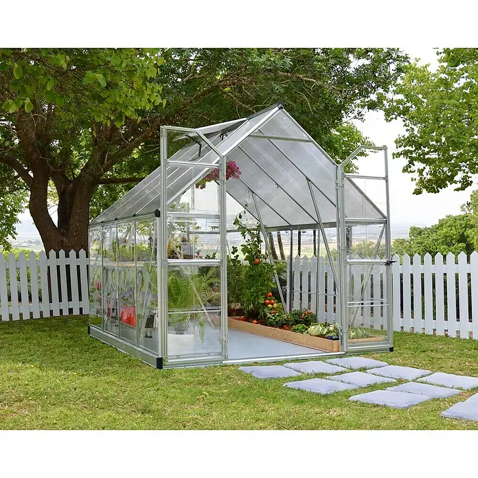 Palram – Canopia Gewächshaus Balance - Außenmaß inkl. Dachüberstand (B x T): 244 x 247 cm, 0,7 mm, Silber - Gewächshaus mit Pflanzen und Gemüse im Garten, umgeben von einem weißen Zaun und Bäumen.
