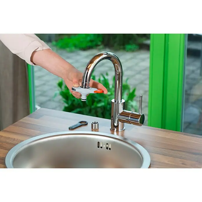 Gardena Hahnstück - Geeignet für: Wasserhähne mit Perlstrahlkopf - Nahaufnahme eines Gardena Wasserhahns mit einer Hand, die den Adapter bedient, auf einem Holztisch mit Spüle.