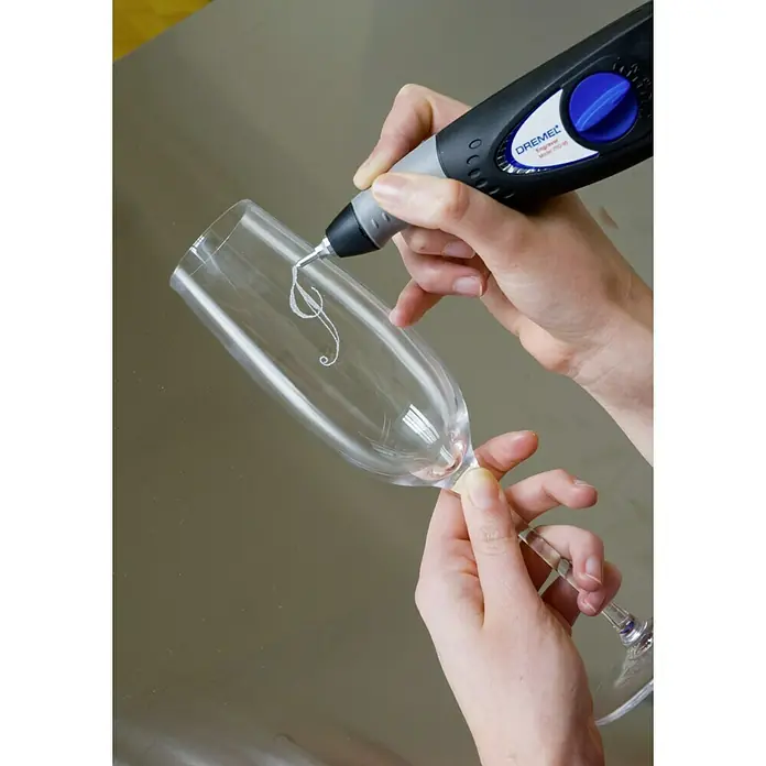 Dremel Graviergerät 290-3 Hobby - 35 W - Eine Person graviert mit einem Dremel-Werkzeug ein florales Design auf ein Champagnerglas, wodurch ein einzigartiges, personalisiertes Geschenk entsteht.