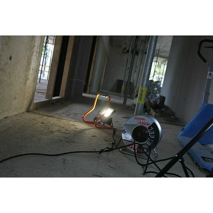 Ledvance LED-Strahler - 30 W, 2.700 lm, 4.000 K, L x B x H: 19 x 22 x 29 cm, IP44 - Aufnahme einer Baustelle mit einer tragbaren Arbeitsleuchte und einer Kabeltrommel mit der Aufschrift "Stahl".