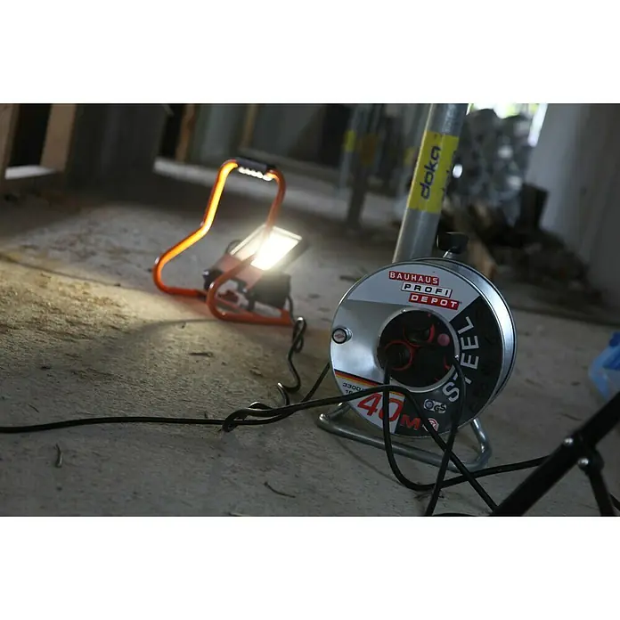 Ledvance LED-Strahler - 30 W, 2.700 lm, 4.000 K, L x B x H: 19 x 22 x 29 cm, IP44 - Ein Baustellenfoto, das eine Kabeltrommel von Bauhaus Profi Depot und eine Arbeitsleuchte zeigt. Die Kabeltrommel ist silberfarben und mit einem Stahlkabel ausgestattet.