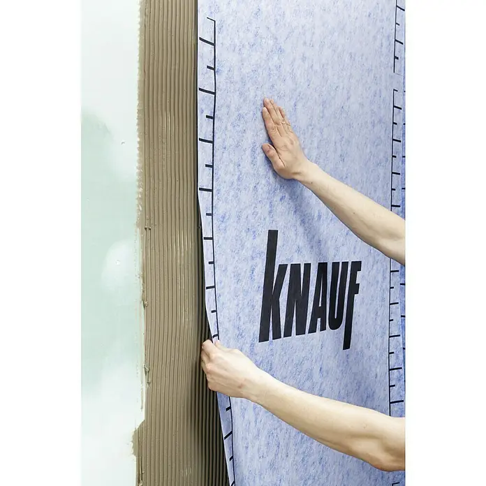 Knauf Abdichtungs-Entkopplungsbahn - 5 m², Polypropylen, Höhe: 0,6 mm - Nahaufnahme der Anbringung einer Knauf Dichtbahn auf eine Wand mit Fliesenkleber, ein wichtiger Schritt im Badezimmerbau für zuverlässigen Feuchtigkeitsschutz.