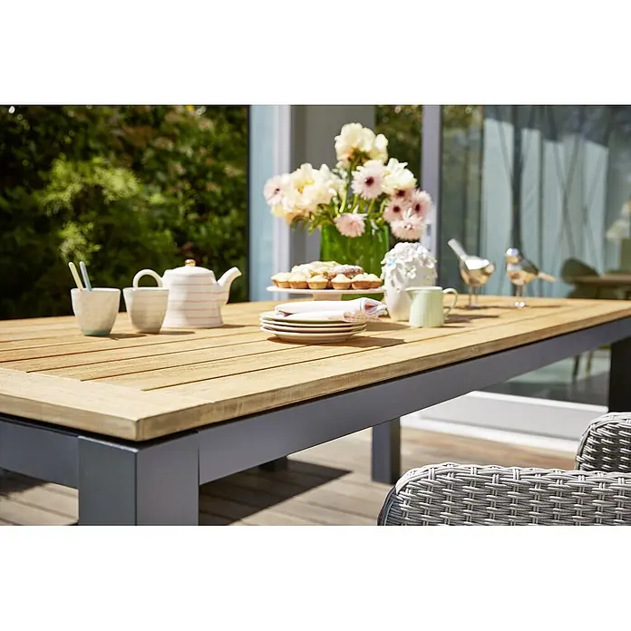Sunfun Gartentisch Lynn - L x B x H: 220 x 100 x 76 cm, Akazie, Aluminium, Teakbraun, Anthrazit - Outdoor-Szene mit einem stilvollen Esstisch, gedeckt mit Geschirr, Gebäck und Blumen. Genießen Sie das Essen im Freien mit Eleganz.