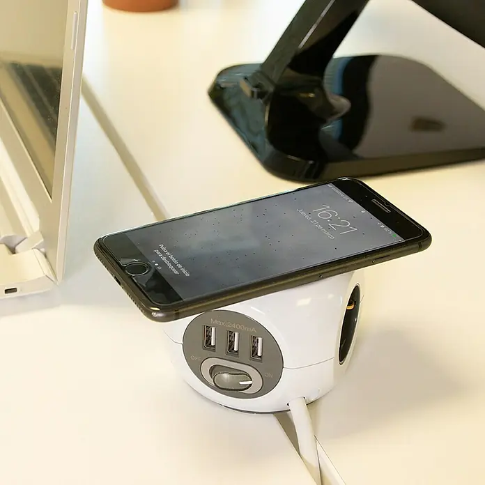 Simon Bola de enchufes con USB + carga inalámbrica Combi Ball - x 3, Blanco, 1,4 m, IP20 - Una regleta blanca con puertos USB y un smartphone están sobre una mesa. Perfecto para cargar varios dispositivos simultáneamente.