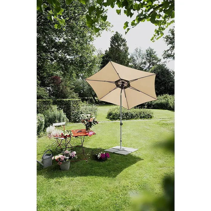 Suncomfort Marktschirm rund Pop Up - Sandweiß, Durchmesser Bespannung: 300 cm - Sonnenschirm auf einer grünen Wiese, der Schatten spendet und zum Verweilen einlädt. Tisch und Stuhl mit Blumenarrangements stehen bereit.