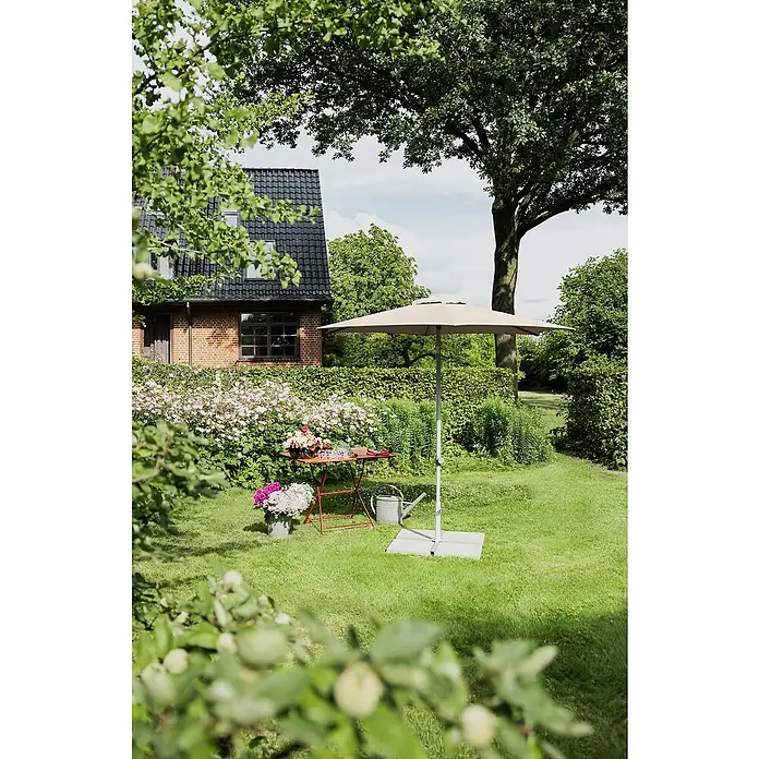 Suncomfort Marktschirm rund Pop Up - Sandweiß, Durchmesser Bespannung: 300 cm - Ein beigefarbener Sonnenschirm mit Ständer steht im Garten neben einem roten Tisch mit Blumen und einer Gießkanne.
