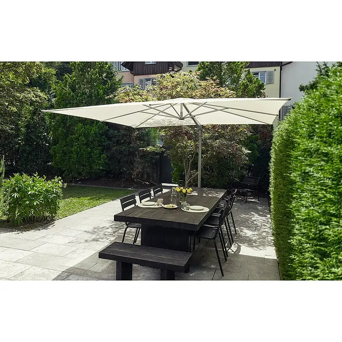 Suncomfort Ampelschirm Sunflex - Light Taupe, Bespannungsmaß (L x B): 300 x 300 cm - Eine große Esstischgarnitur mit Sonnenschirm steht auf einer Terrasse, umgeben von üppigem Grün. Der Tisch ist gedeckt und lädt zum Verweilen ein.