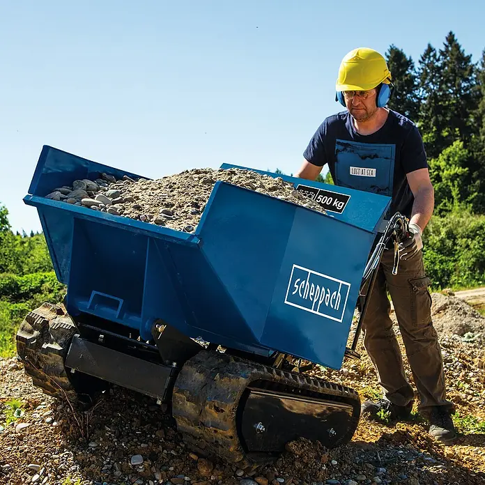 Scheppach Kettendumper DP 5000 - Motorbetrieben, Fassungsvermögen: 125 l, Traglast: 500 kg - Der Scheppach Mini-Dumper mit Raupenantrieb ist mit Kies beladen und wird von einem Arbeiter bedient, der Schutzkleidung trägt.