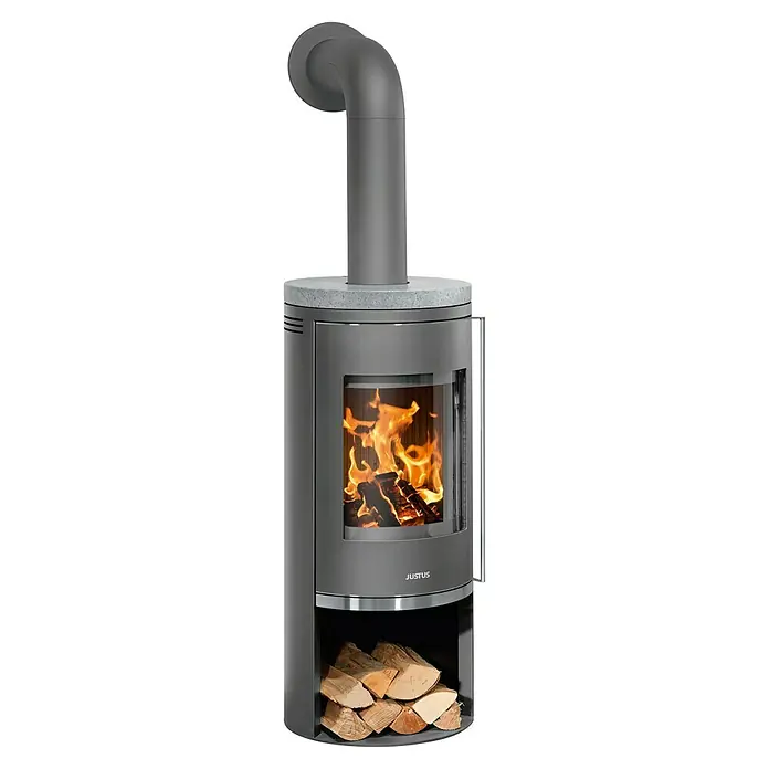 Justus Kaminofen Faro 2.0 - 6 kW, Raumheizvermögen: 115 m³, Verkleidung: Gusseisen/Speckstein, Speckstein - Justus Kaminofen: Ein grauer Kaminofen mit Glasfront, in dem ein Feuer brennt. Holzscheite sind im unteren Fach gelagert, und ein Rauchrohr führt nach oben.