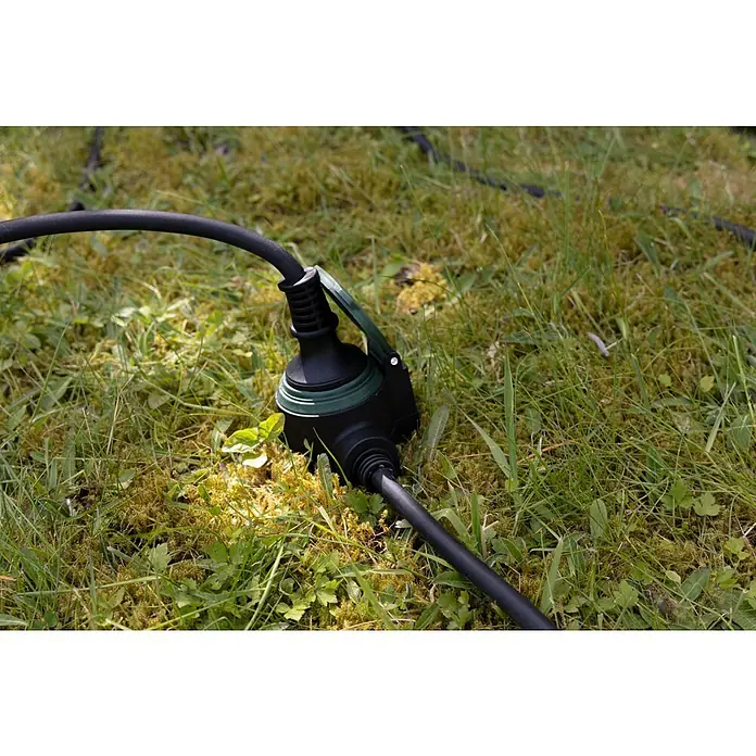 REV Verlängerungskabel - 10 m, Grün / Schwarz, IP44, H07RN-F - Stromverteiler auf einer Wiese. Der Verteiler ist schwarz mit einem grünen Ring und verbunden mit einem Stromkabel.