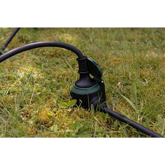 REV Verlängerungskabel - 10 m, Grün / Schwarz, IP44, H07RN-F - Nahaufnahme einer schwarzen, wasserdichten Steckdose mit grünem Akzent auf einer grünen Rasenfläche mit einem schwarzen Kabel.