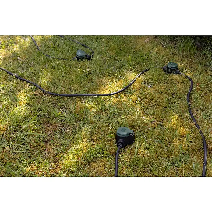 REV Verlängerungskabel - 10 m, Grün / Schwarz, IP44, H07RN-F - Eine Nahaufnahme von drei grünen, wasserdichten Stromverteilern, die mit schwarzen Kabeln auf einer Wiese mit gelbem Moos verbunden sind.