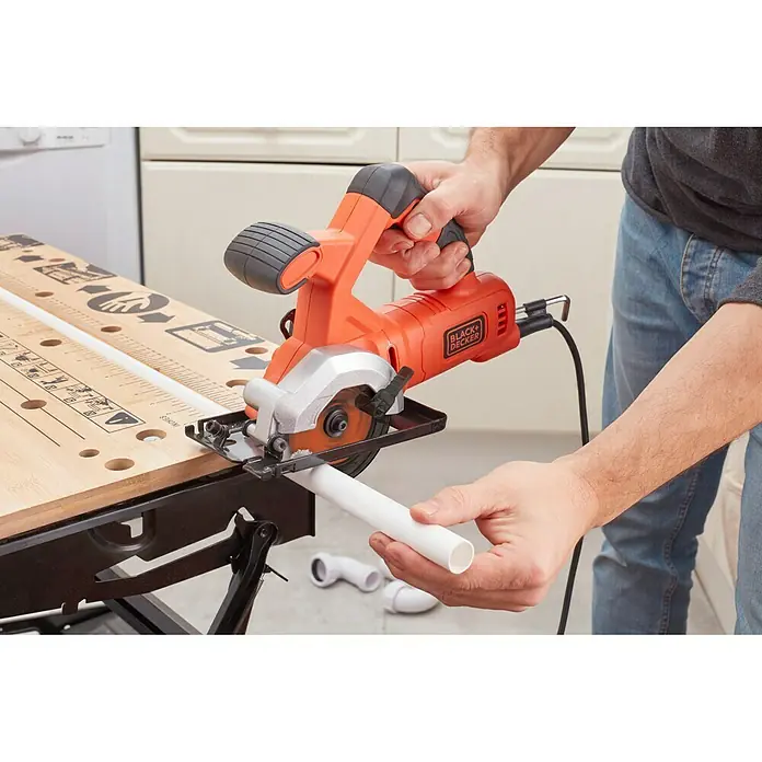 Black+Decker Minisierra circular de mano BES510-QS - 400 W, Diámetro hoja de sierra: 85 mm, Número de revoluciones de marcha en vacío: 3.600 r.p.m. - Primer plano de una sierra circular Black+Decker cortando un tubo de PVC en un banco de trabajo, ideal para bricolaje.