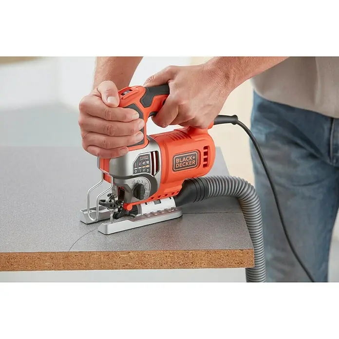 Black+Decker Sierra de calar eléctrica BES610K-QS - 1.000 /min - 3.100 /min, 90 mm - Primer plano de una sierra de calar Black+Decker en acción, cortando un trozo de madera, operada por una persona en jeans.