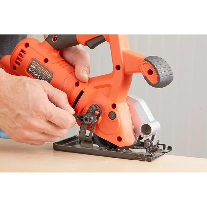 Black+Decker Minisierra circular de mano BES510-QS - 400 W, Diámetro hoja de sierra: 85 mm, Número de revoluciones de marcha en vacío: 3.600 r.p.m. - Primer plano de una sierra circular Black+Decker, en naranja y negro, sobre una mesa de madera y accionada por una persona.