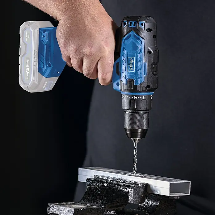 Scheppach IXES 20V Akku-Bohrschrauber C-DD45-X - 20 V, Ohne Akku, 45 Nm - Akkubohrer von Scheppach beim Bohren eines Metallstücks, das in einem Schraubstock befestigt ist. Das blaue und schwarze Design sticht hervor.
