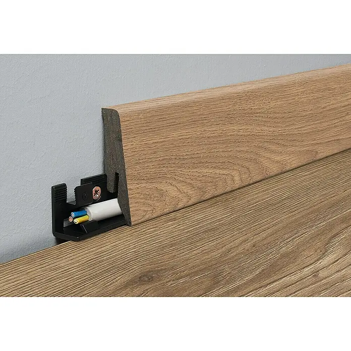 LOGOCLIC Aquaprotect Sockelleiste K58 C Piton Oak - 2,6 m x 18 mm x 58 mm, HDF - Die Bild zeigt eine Holzfußleiste mit integriertem Kabelkanal und installierten Elektrokabeln an einer Wand.
