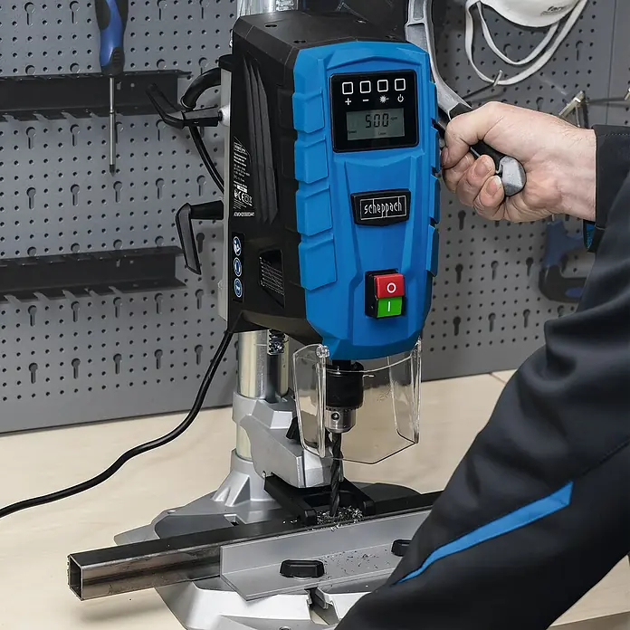 Scheppach Tischbohrmaschine DP55 - 710 W, Leerlaufdrehzahl: 500 U/min - 2.600 U/min, Spannweite Bohrfutter: 1,5 mm - 13 mm - Eine Scheppach Tischbohrmaschine beim Bohren eines Metallstücks, bedient von einer Person.