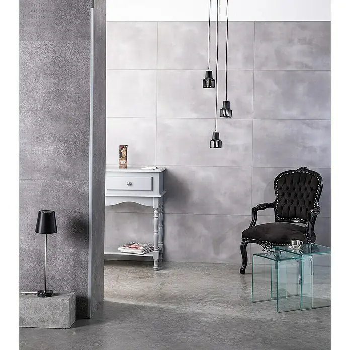 Grosfillex Wall+ Wandpaneel - Grey Cement, 900 x 450 x 5 mm - Elegantes Interieur mit grauen Fliesen, einem schwarzen Sessel und einer stilvollen Lampe. Das perfekte Ambiente für moderne Wohnräume.