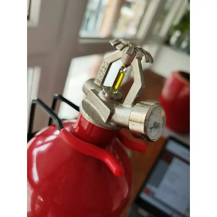 Extintor de incendios - 2 kg, Polvo - Primer plano de un extintor rojo con una pieza plateada que contiene un líquido amarillo.