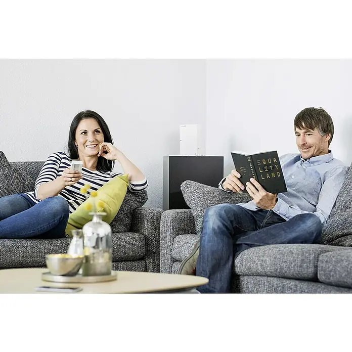 Schellenberg Temporizador inalámbrico Premium - Sistemas soportados: Sistema Smart Home Schellenberg, Apto para: 25 motores telecontrolados - Una mujer con un mando a distancia y un hombre leen el libro "Equality Land" sentados en un sofá.