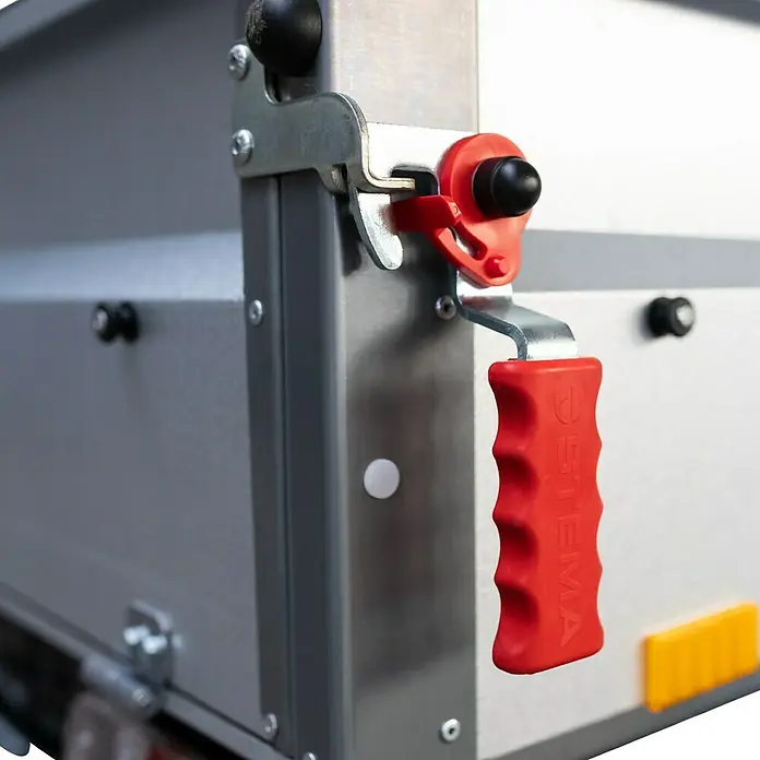 Stema Anhänger BASIC STL 1000-21-13 - Nutzlast: 781 kg, Einachser, Kasteninnenmaß: 210 x 128 x 35 cm, Gebremst - Nahaufnahme des Verriegelungsmechanismus eines Anhängers mit einem roten Griff.