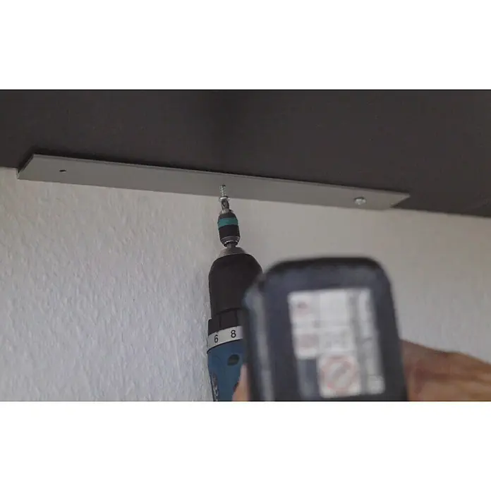 Easy Connect Montagewinkel - Passend für: Easy Connect Regalsystem, 3 Stk. - Ein Akkuschrauber befestigt eine silberne Metallschiene an einer dunklen Oberfläche, möglicherweise eine Decke oder ein Regal, mit einer Schraube.