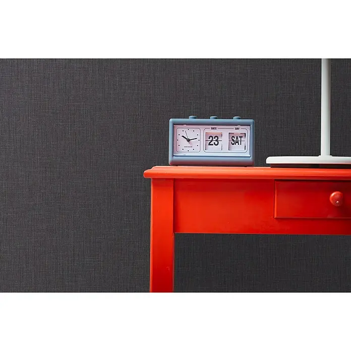 A.S. Création Metropolitan Stories Vliestapete Textiloptik - Anthrazit, Uni, 10,05 x 0,53 m - Ein auffälliger orangefarbener Tisch mit einem Retro-Flip-Kalender, der den 23. Samstag anzeigt, unterstreicht den Vintage-Charme des Produkts.