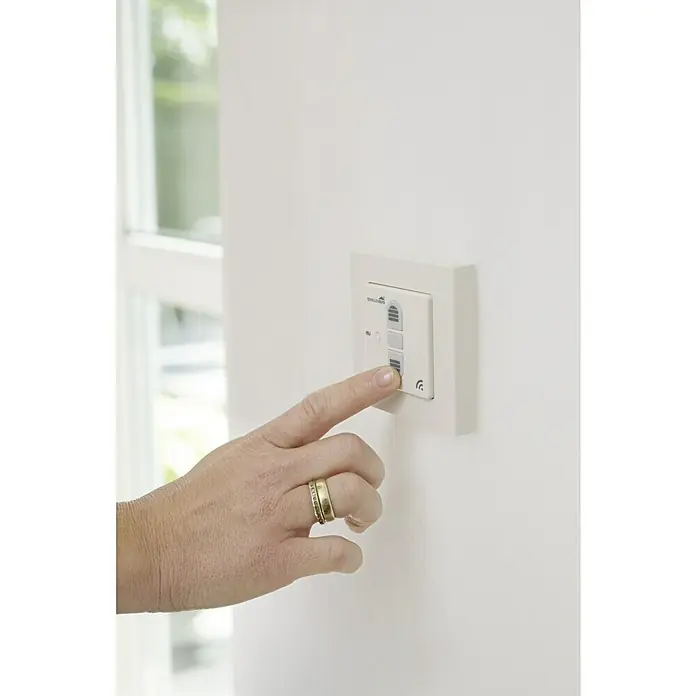 Schellenberg Smart Home Interruptor de recepción por radio - 80 x 80 x 40 mm, Blanco, Montaje enrasado - Una mano presiona un botón en un sistema de control de persianas enrollables blanco montado en una pared junto a una ventana.