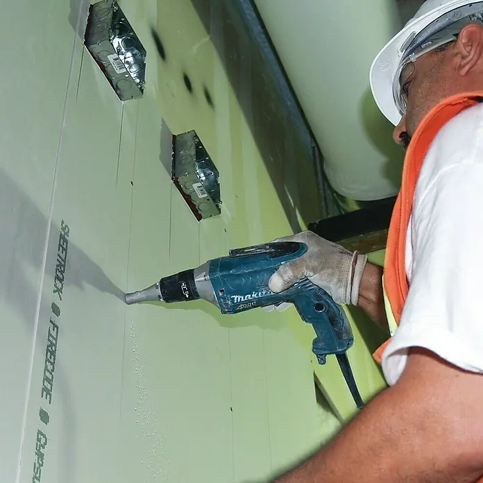 Makita Atornillador para placas de yeso FS4200 - 570 W, 4.000 r.p.m. - Un trabajador de la construcción está usando un atornillador para paneles de yeso Makita para fijar una lámina de paneles de yeso a una pared.