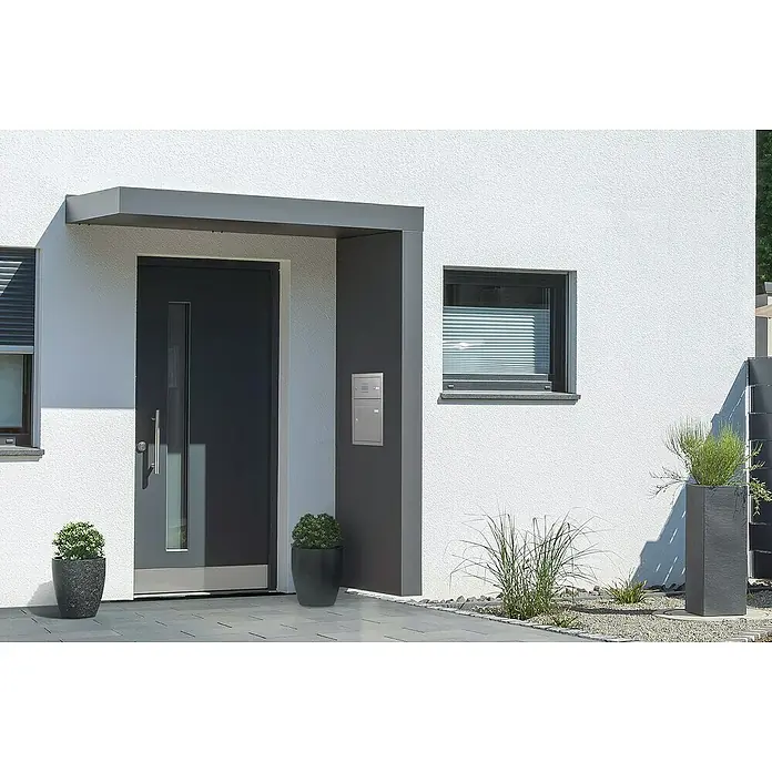 Gutta Rechteckvordach BS Plus 200 UP ST BK FUKA - 200 x 90 x 15,5 cm, Seitenteil rechts, Briefkastenanlage Edelstahl - Eine moderne Haustür mit grauer Fassade, minimalistischem Design und Pflanzenkübeln. Die Tür zeichnet sich durch ihre schlichte Eleganz aus.