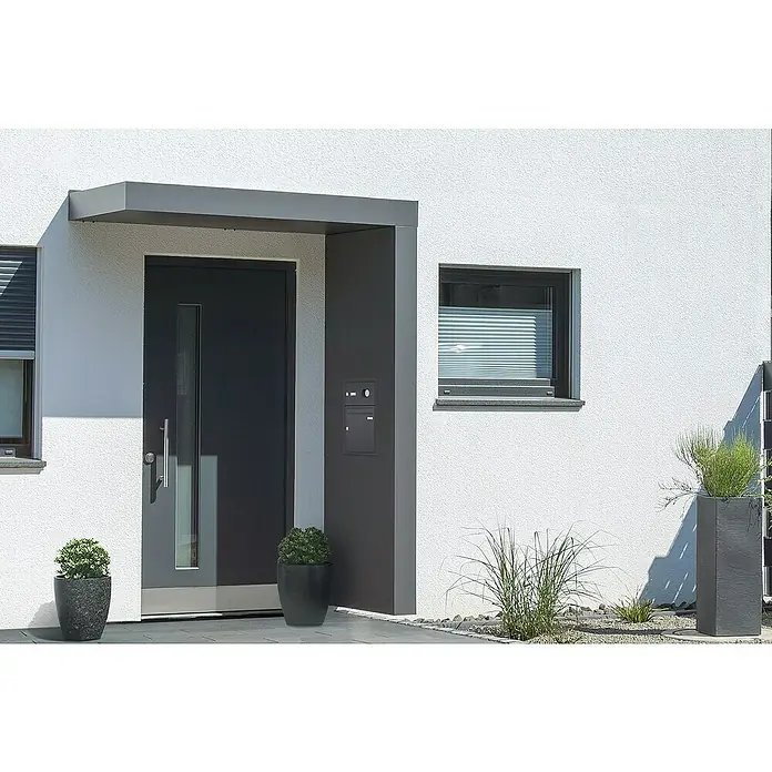 Gutta Rechteckvordach BS Plus 200 UP ST BK Video - 200 x 90 x 15,5 cm, Seitenteil rechts, Briefkastenanlage Anthrazit mit Video-Funktion - Eine moderne Haustür in Anthrazit mit einem schmalen Fenster und einem grauen Vordach, flankiert von Pflanzenkübeln und einer Briefkastenanlage.