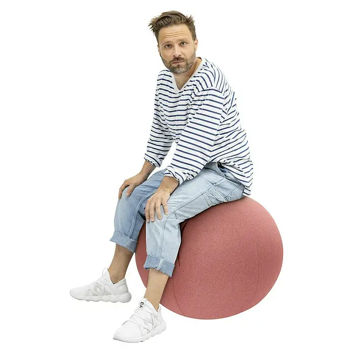 Sitting Ball Gymnastikball Felt - Lachs, Durchmesser: 65 cm, 100 % Polyester - Ein Mann sitzt auf einem Gymnastikball, der als ergonomischer Bürostuhl dient. Er trägt ein gestreiftes Hemd und Jeans.