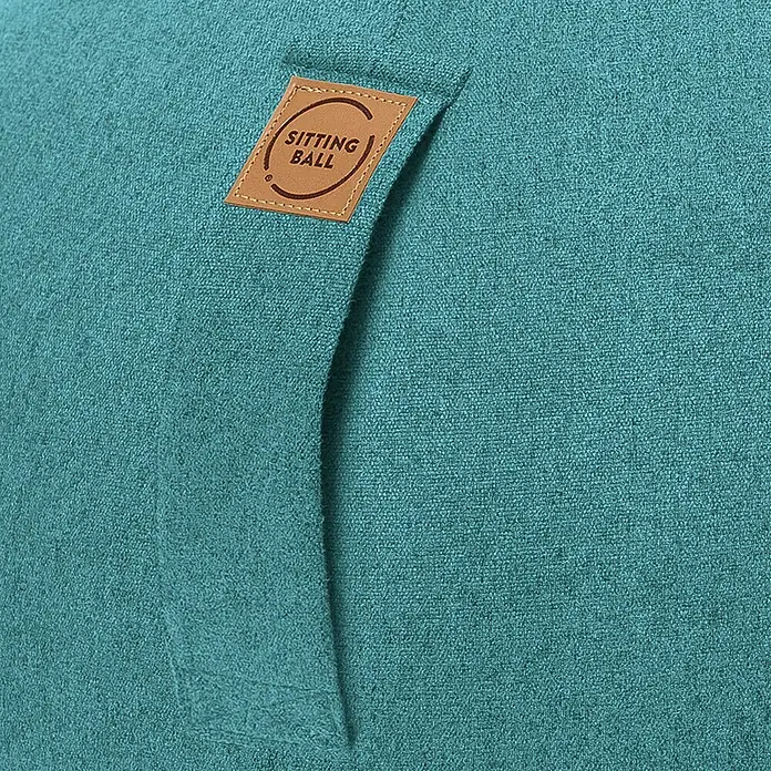 Sitting Ball Gymnastikball Felt - Aquarius, Durchmesser: 65 cm, 100 % Polyester - Nahaufnahme eines Sitzballs mit einem braunen Lederetikett, auf dem "Sitting Ball" steht, vor einem türkisfarbenen Hintergrund.