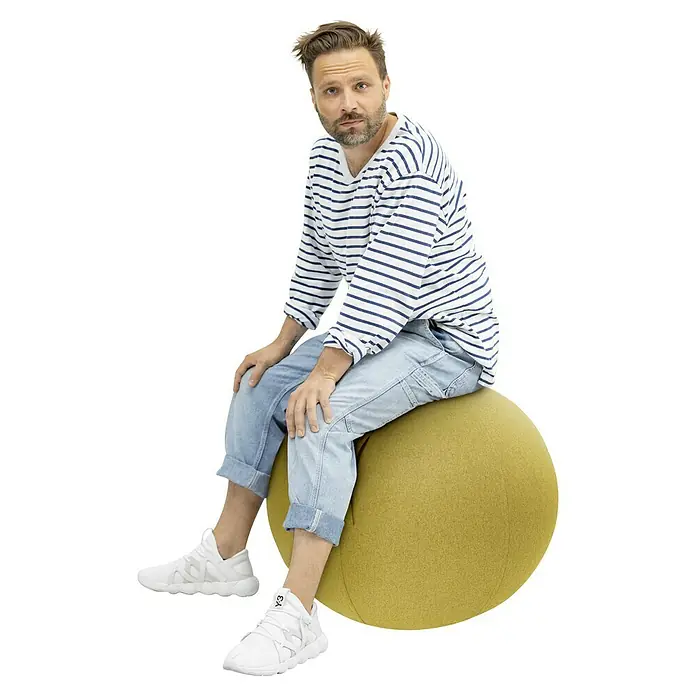 Sitting Ball Gymnastikball Felt - Senf, Durchmesser: 65 cm, 100 % Polyester - Ein Mann sitzt auf einem gelben Sitzball, der sich ideal für dynamisches Sitzen und eine gesunde Körperhaltung eignet. Der Ball fördert Bewegung und stärkt die Rückenmuskulatur.