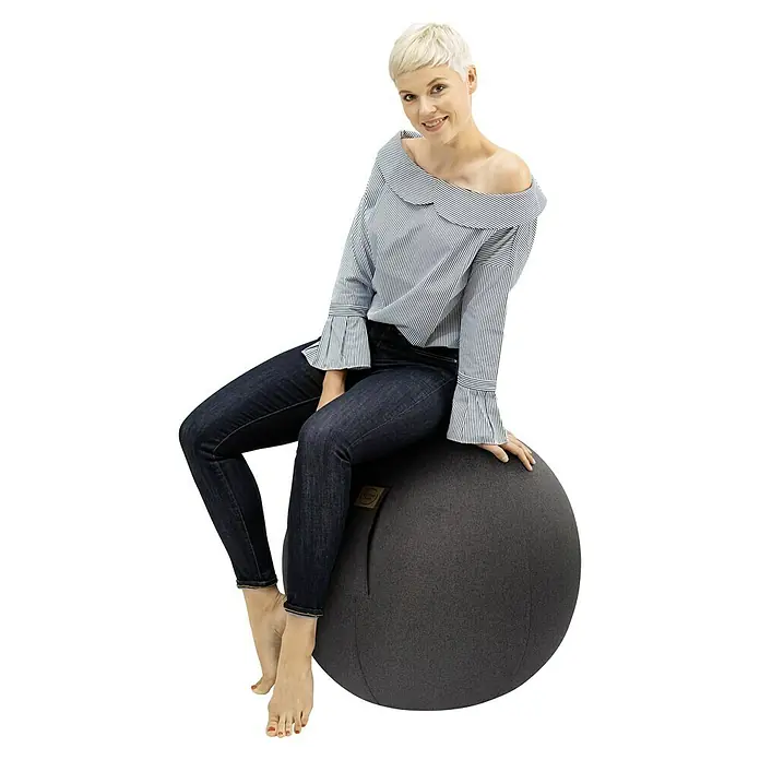 Sitting Ball Gymnastikball Felt - Anthrazit, Durchmesser: 65 cm, 100 % Polyester - Eine Frau sitzt auf einem grauen Gymnastikball. Der Ball ist ein bequemer und stilvoller Sitzball für zu Hause oder das Büro.