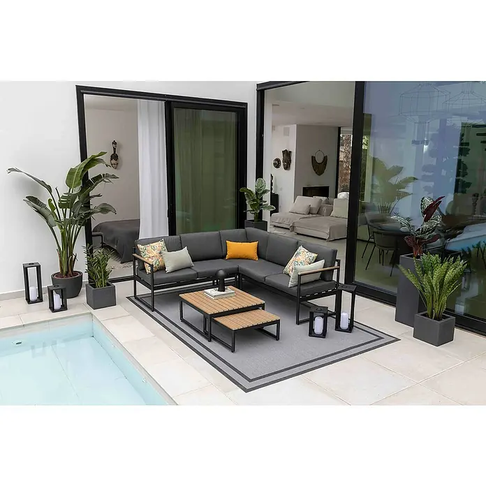 Sunfun Conjunto de muebles Eliane - 5 pzs., Aluminio/Polywood, Antracita - Elegante salón de jardín gris con mesa de centro sobre una alfombra elegante, rodeado de exuberantes plantas e iluminación moderna.