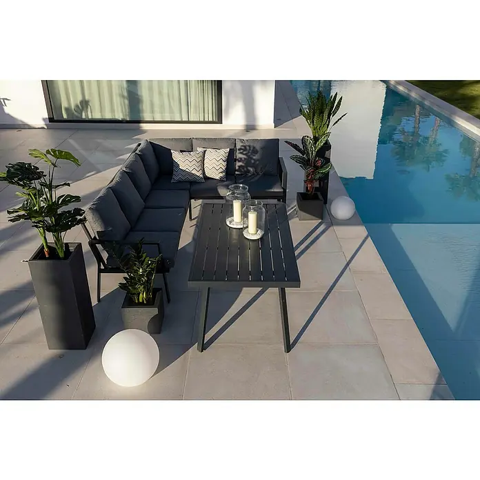 Conjunto de muebles Freya - 3 pzs., Aluminio, Antracita - Una acogedora área exterior con un sofá de esquina gris, una mesa con velas y vegetación exuberante, ideal para la relajación al aire libre.