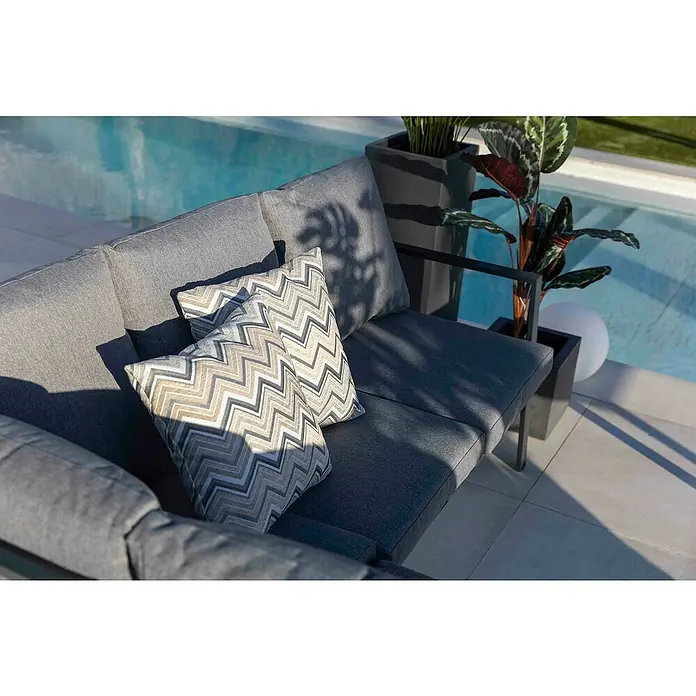 Conjunto de muebles Freya - 3 pzs., Aluminio, Antracita - Primer plano de un sofá gris con cojines en zigzag, una planta y una piscina al fondo.