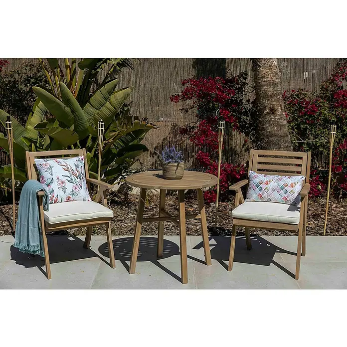 Sunfun Conjunto de muebles de balcón Siena - 3 pzs., Madera de acacia, Marrón - Agradable escena de jardín con un conjunto de asientos de madera con dos sillas y una mesa redonda, rodeada de exuberante vegetación.